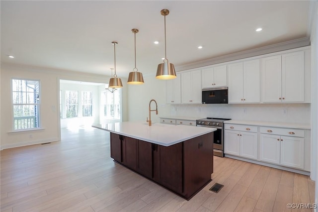 kitchen featuring an island with sink, decorative light fixtures, electric range, sink, and white cabinetry