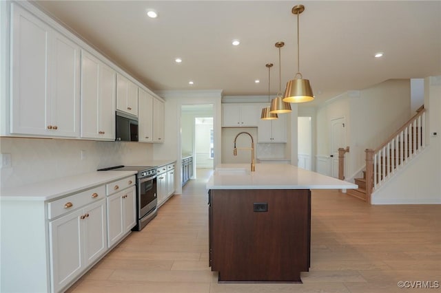 kitchen with white cabinetry, appliances with stainless steel finishes, an island with sink, and pendant lighting