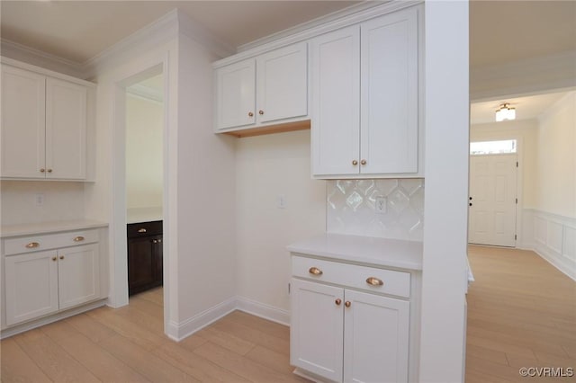 kitchen featuring white cabinets, light wood-type flooring, crown molding, and tasteful backsplash