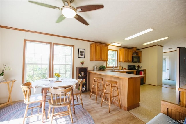 kitchen featuring range with electric stovetop, crown molding, a breakfast bar area, and kitchen peninsula