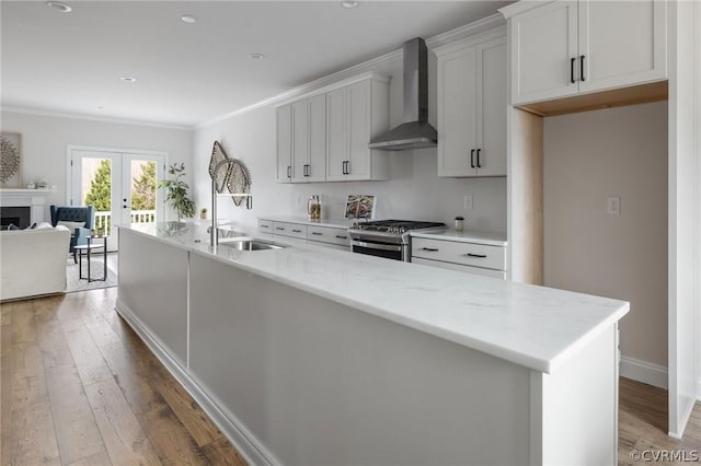 kitchen with gas range, light stone countertops, sink, wall chimney exhaust hood, and an island with sink