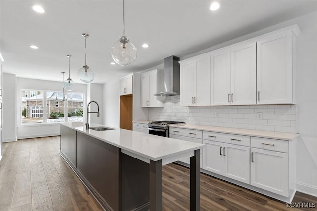 kitchen featuring wall chimney range hood, decorative light fixtures, gas stove, sink, and white cabinetry