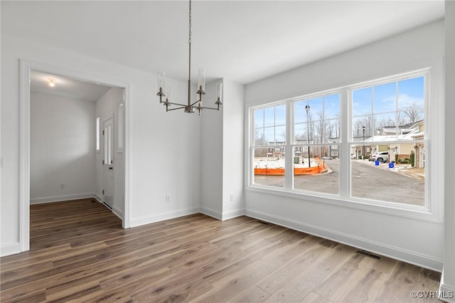 unfurnished dining area with plenty of natural light, an inviting chandelier, and wood-type flooring