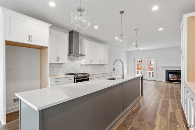 kitchen with gas range, a kitchen island with sink, hanging light fixtures, sink, and wall chimney exhaust hood