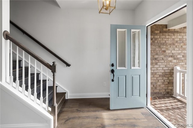 foyer entrance featuring hardwood / wood-style floors, brick wall, and a chandelier