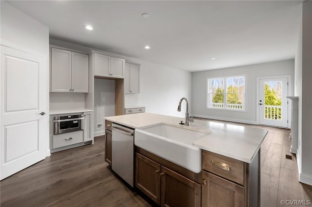 kitchen with stainless steel appliances, a kitchen island with sink, dark wood-type flooring, and sink