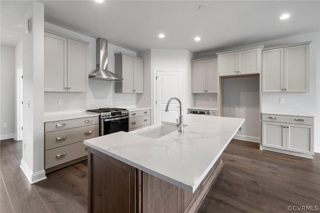 kitchen with light stone countertops, sink, wall chimney range hood, a kitchen island with sink, and stainless steel range with gas stovetop