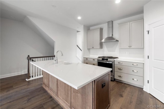 kitchen featuring gray cabinetry, a kitchen island with sink, sink, wall chimney range hood, and stainless steel range with gas cooktop