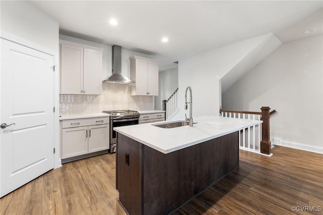 kitchen with a center island with sink, gas stove, wood-type flooring, sink, and wall chimney range hood