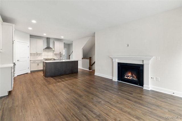 kitchen featuring backsplash, dark hardwood / wood-style flooring, wall chimney exhaust hood, white cabinets, and an island with sink