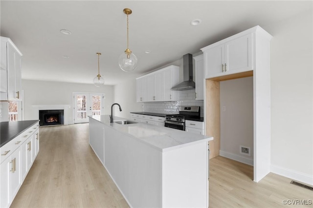 kitchen featuring sink, stainless steel gas range oven, dark stone countertops, wall chimney exhaust hood, and pendant lighting