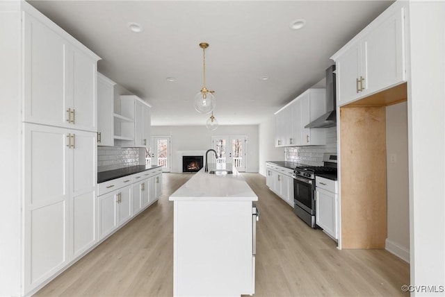 kitchen with a center island with sink, gas stove, pendant lighting, wall chimney exhaust hood, and white cabinets