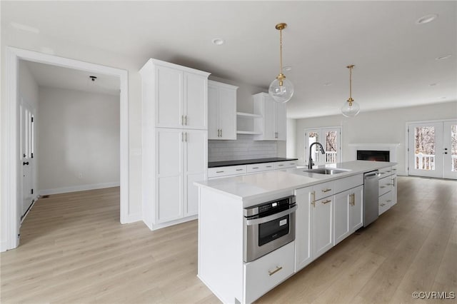 kitchen with an island with sink, decorative light fixtures, sink, appliances with stainless steel finishes, and white cabinets