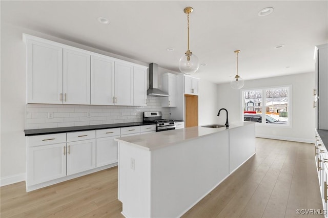 kitchen with an island with sink, decorative light fixtures, stainless steel range with gas stovetop, sink, and wall chimney exhaust hood