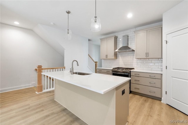 kitchen with a center island with sink, light hardwood / wood-style flooring, sink, pendant lighting, and wall chimney exhaust hood