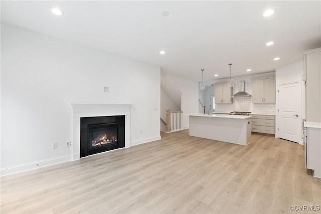 kitchen with an island with sink, decorative light fixtures, light hardwood / wood-style floors, wall chimney range hood, and decorative backsplash