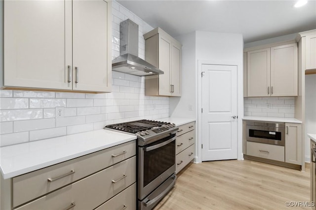 kitchen featuring wall chimney range hood, light wood-type flooring, gas stove, and backsplash