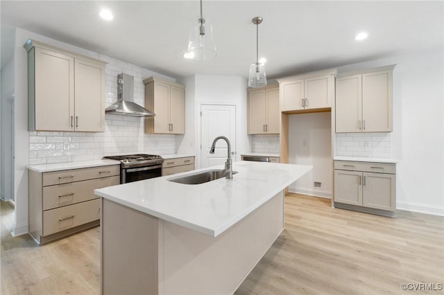 kitchen with a center island with sink, hanging light fixtures, sink, stainless steel gas stove, and wall chimney exhaust hood