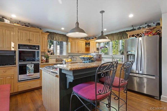 kitchen featuring light stone counters, stainless steel fridge, a kitchen island, double oven, and a breakfast bar