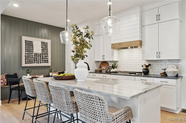 kitchen featuring hanging light fixtures, a kitchen island with sink, white cabinets, and a kitchen breakfast bar