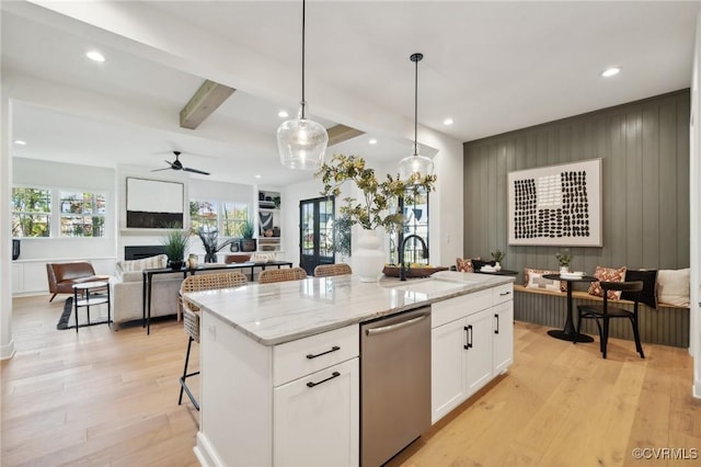 kitchen featuring sink, a breakfast bar area, white cabinetry, stainless steel dishwasher, and a kitchen island with sink