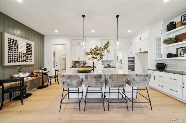 kitchen featuring white cabinetry, a breakfast bar, hanging light fixtures, and a center island with sink