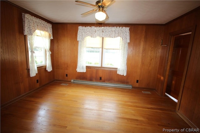 spare room featuring a baseboard heating unit, ceiling fan, wood walls, and light wood-style floors