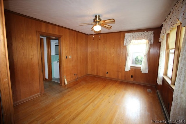 spare room featuring visible vents, baseboard heating, ornamental molding, wooden walls, and wood finished floors