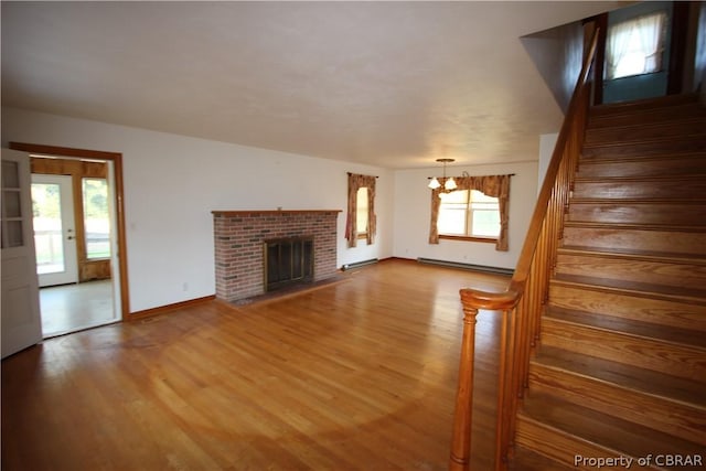 unfurnished living room featuring a fireplace, stairway, an inviting chandelier, and wood finished floors