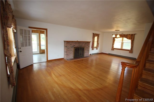 unfurnished living room featuring a baseboard radiator, a fireplace, light wood finished floors, and an inviting chandelier