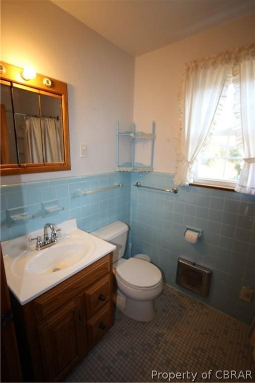 full bathroom with toilet, a wainscoted wall, tile patterned floors, vanity, and tile walls