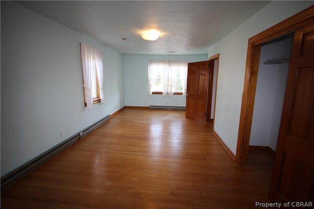 unfurnished bedroom featuring a baseboard heating unit, light wood-type flooring, and baseboards