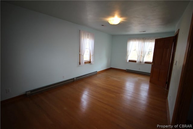 spare room featuring a baseboard heating unit, a healthy amount of sunlight, baseboard heating, and wood finished floors