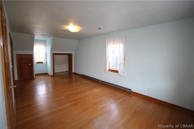 unfurnished room featuring light wood finished floors, vaulted ceiling, baseboards, and baseboard heating