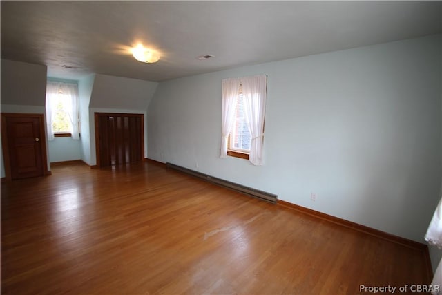 additional living space featuring a baseboard heating unit, light wood-type flooring, visible vents, and baseboards