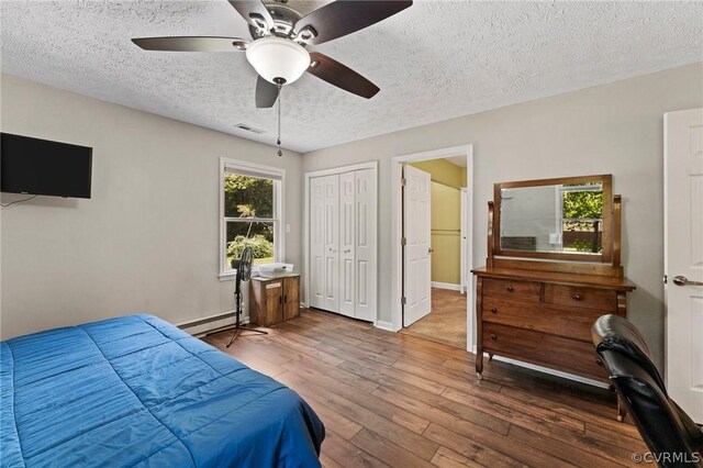 bedroom with a closet, a baseboard heating unit, a textured ceiling, ceiling fan, and wood-type flooring