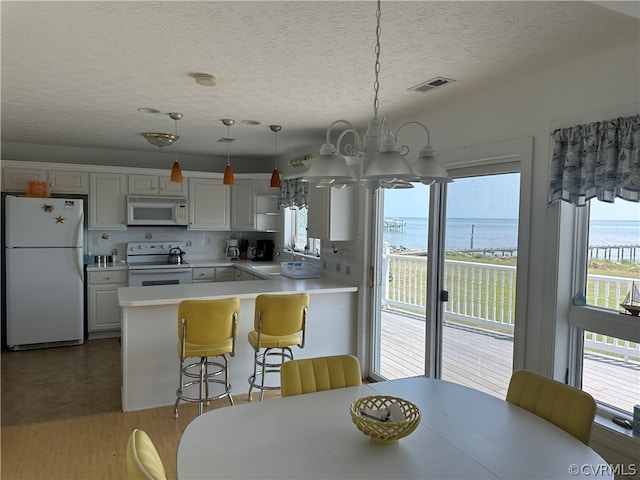 dining area featuring visible vents, a water view, a chandelier, light wood-type flooring, and a textured ceiling