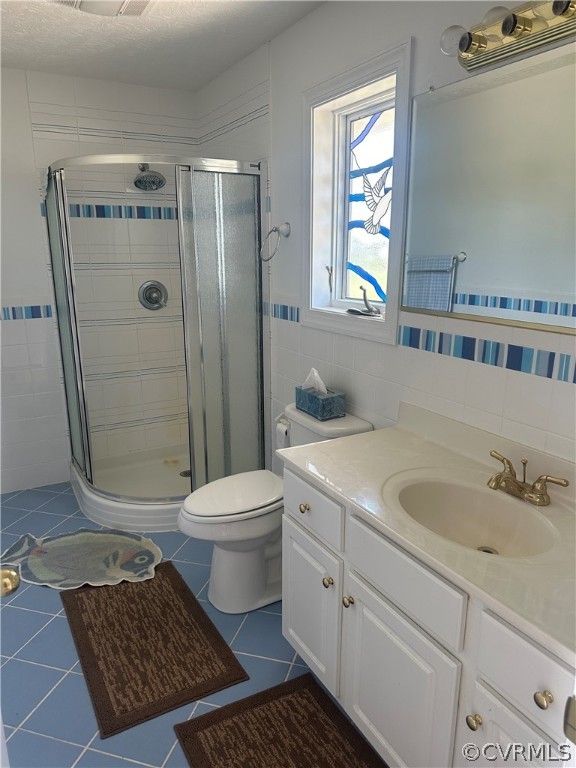 full bathroom featuring toilet, vanity, a stall shower, tile patterned floors, and tile walls