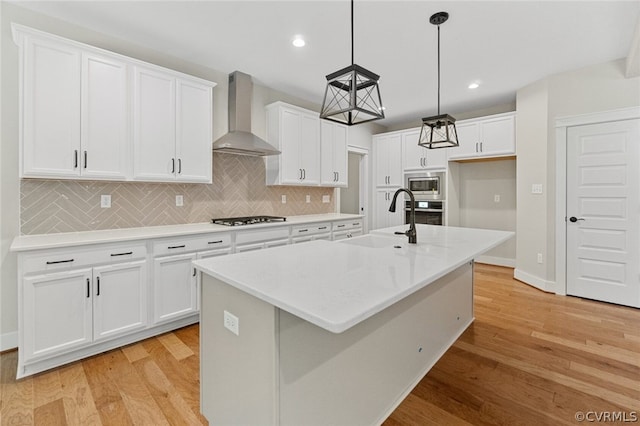 kitchen featuring a sink, white cabinetry, stainless steel appliances, light wood-style floors, and wall chimney range hood