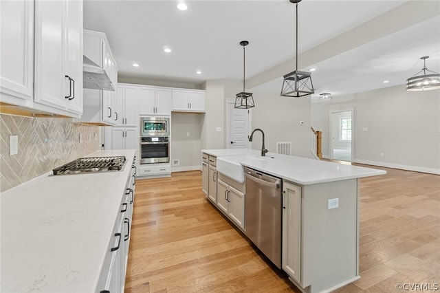 kitchen with light wood-style flooring, wall chimney exhaust hood, appliances with stainless steel finishes, and a sink