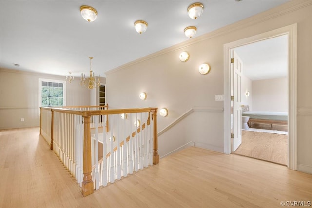 hallway featuring crown molding, baseboards, a chandelier, an upstairs landing, and wood finished floors