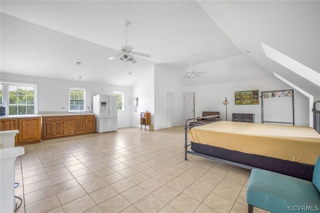 bedroom with light tile patterned flooring, lofted ceiling with skylight, white refrigerator with ice dispenser, and a ceiling fan