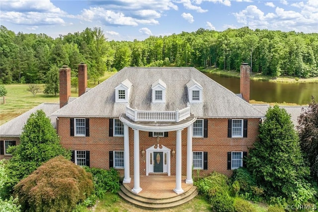 neoclassical / greek revival house with a water view, brick siding, a wooded view, and a chimney