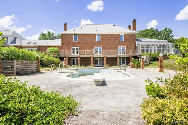 rear view of property with an outdoor pool, a wooden deck, brick siding, a chimney, and a patio area