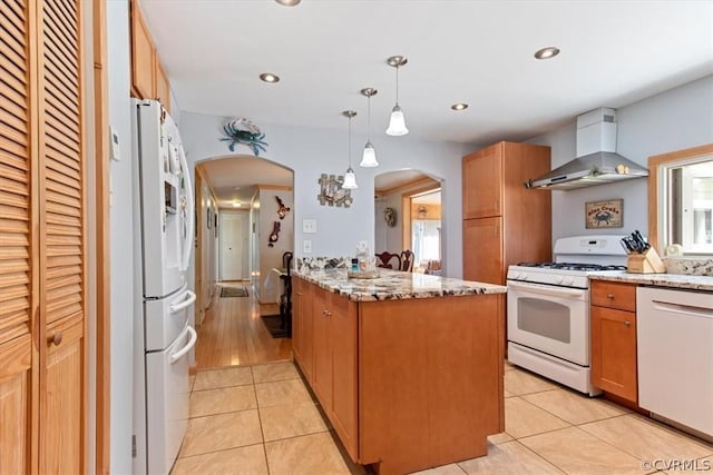 kitchen with light stone countertops, hanging light fixtures, wall chimney range hood, white appliances, and light tile patterned floors