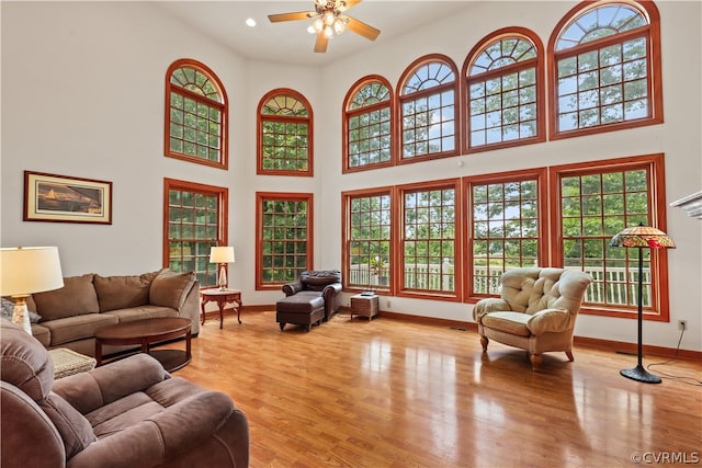 living room with a towering ceiling, ceiling fan, and light wood-type flooring