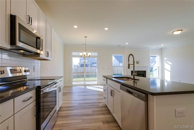 kitchen with appliances with stainless steel finishes, sink, white cabinets, hanging light fixtures, and a kitchen island with sink