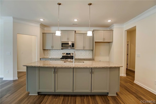 kitchen featuring light stone counters, tasteful backsplash, hanging light fixtures, appliances with stainless steel finishes, and an island with sink