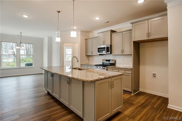 kitchen featuring sink, hanging light fixtures, light stone counters, stainless steel appliances, and a center island with sink