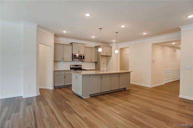 kitchen featuring appliances with stainless steel finishes, gray cabinetry, hanging light fixtures, light stone counters, and a center island with sink